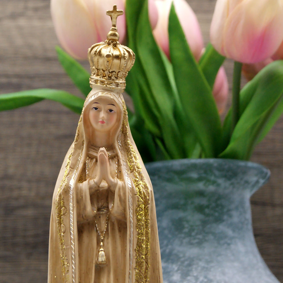 This Our Lady of Fatima statue is made in Fatima, Portugal by the hands of the same artisans that craft the statues of the Shrine of Fatima. The impressive craftsmanship and attention to detail give it a wooden look-alike appearance, although it's made from resin. The figurine sits on a cloud and shows Our Lady wearing a mantle with golden accents painted by hand. On the bottom of the statue it has a music box operated by batteries that plays the Fátima Hymn, Ave.