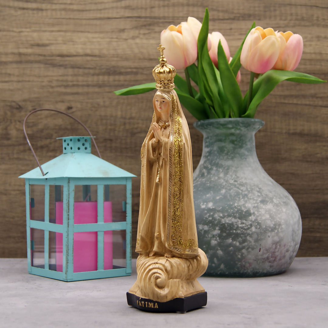 This Our Lady of Fatima statue is made in Fatima, Portugal by the hands of the same artisans that craft the statues of the Shrine of Fatima. The impressive craftsmanship and attention to detail give it a wooden look-alike appearance, although it's made from resin. The figurine sits on a cloud and shows Our Lady wearing a mantle with golden accents painted by hand. On the bottom of the statue it has a music box operated by batteries that plays the Fátima Hymn, Ave.