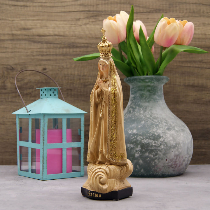 This Our Lady of Fatima statue is made in Fatima, Portugal by the hands of the same artisans that craft the statues of the Shrine of Fatima. The impressive craftsmanship and attention to detail give it a wooden look-alike appearance, although it's made from resin. The figurine sits on a cloud and shows Our Lady wearing a mantle with golden accents painted by hand. On the bottom of the statue it has a music box operated by batteries that plays the Fátima Hymn, Ave.
