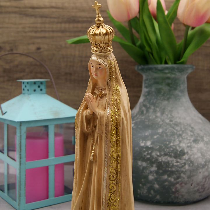 This Our Lady of Fatima statue is made in Fatima, Portugal by the hands of the same artisans that craft the statues of the Shrine of Fatima. The impressive craftsmanship and attention to detail give it a wooden look-alike appearance, although it's made from resin. The figurine sits on a cloud and shows Our Lady wearing a mantle with golden accents painted by hand. On the bottom of the statue it has a music box operated by batteries that plays the Fátima Hymn, Ave.