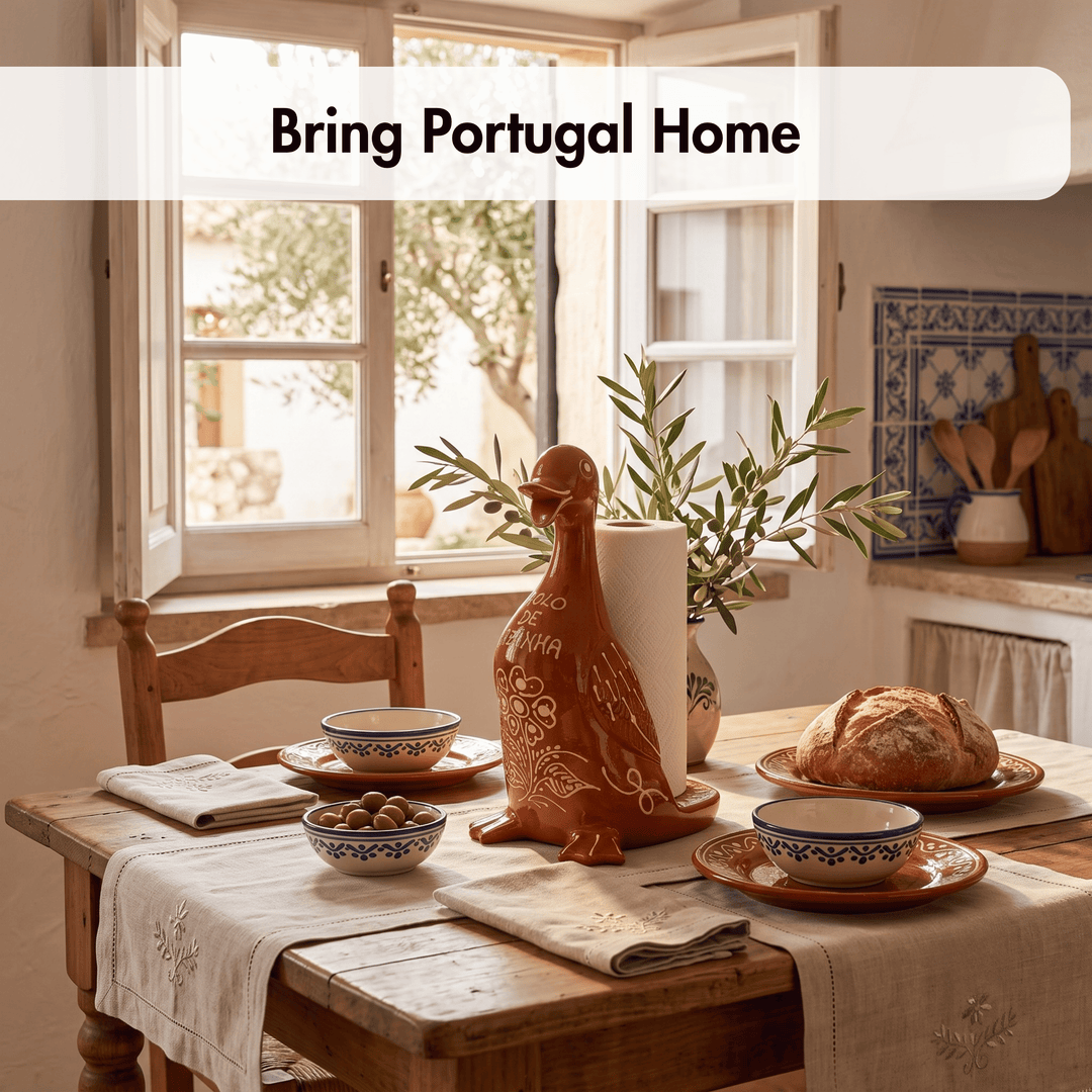 A rustic dining table set in a warm kitchen or dining room, featuring a terracotta-colored ceramic duck-shaped holder with a roll of white paper towels, blue-and-white patterned bowls, a loaf of bread, and a table runner. A white banner at the top reads &