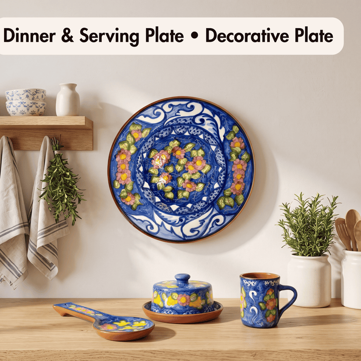 A decorative ceramic dinner plate with a blue and white floral pattern hangs on a wall above a matching serving set including a lidded dish, spoon, and mug. The scene is styled with small plants, towels, and kitchen accessories, and the text &