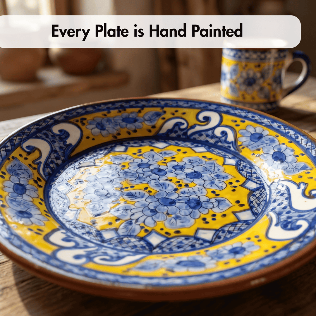 A hand-painted ceramic plate with a vibrant yellow, blue, and white floral pattern, shown on a rustic wooden table with a blurred matching mug in the background. A text overlay at the top reads &