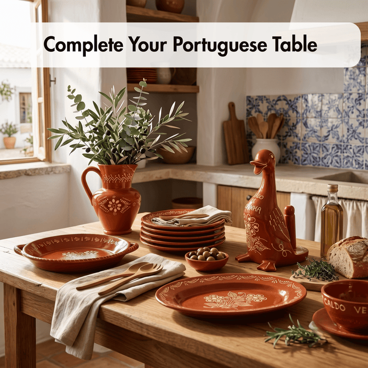 A styled dining table set with terracotta-colored ceramic tableware in a warm kitchen setting. Visible items include oval and round plates, a stack of plates, a duck-shaped utensil holder, a pitcher with greenery, napkins, olives, bread, and a bottle, with the text overlay &