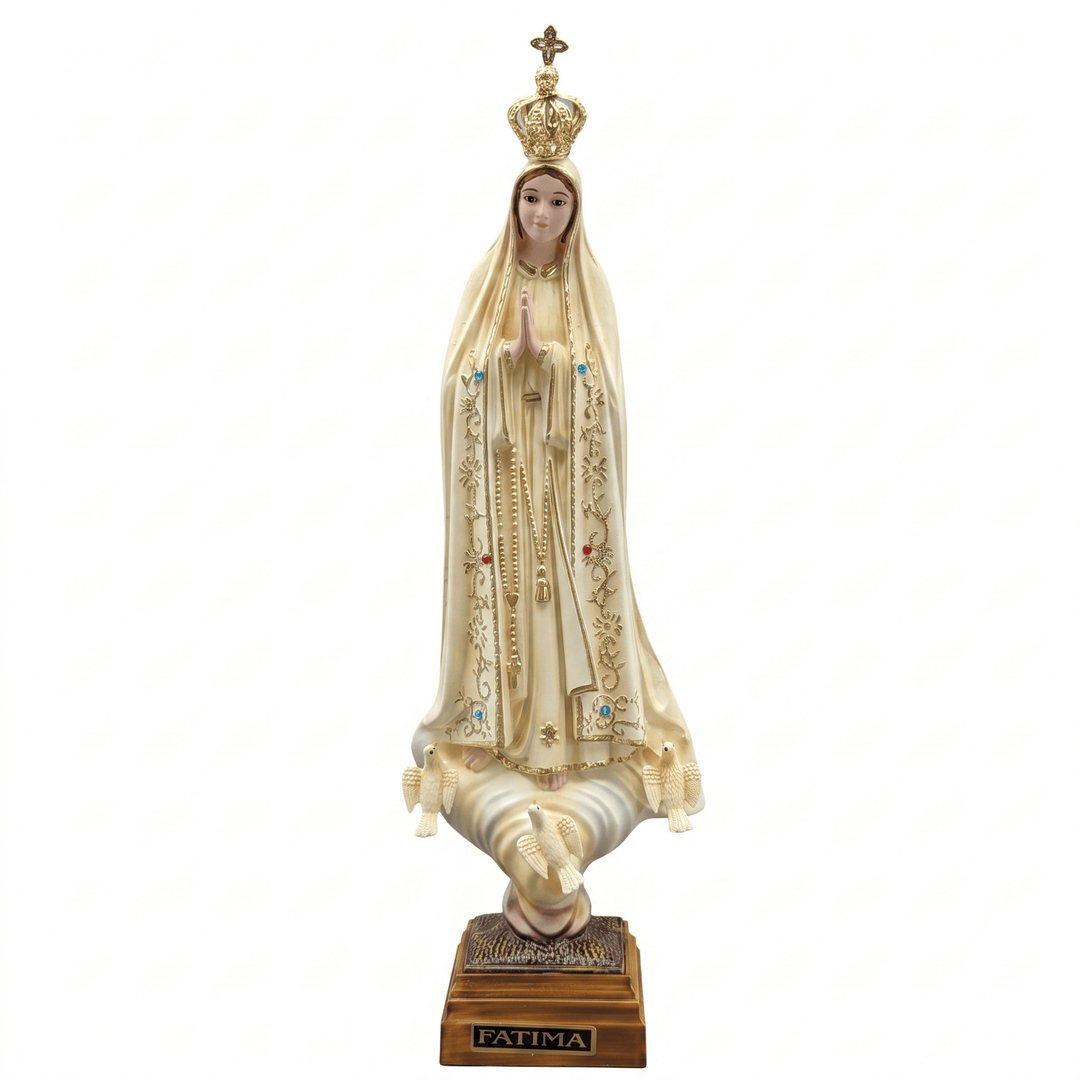 A religious statue of Our Lady of Fatima (Virgen de Fatima) standing on a pair of praying hands atop a wooden base labeled 'PATIMA'. The figure is dressed in an ivory mantle with gold embroidery and a gold crown, set against a plain white background.