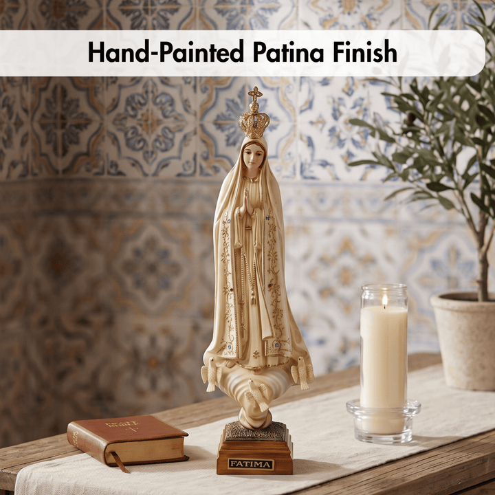 A hand-painted Virgin Mary figurine with a patina finish, displayed on a wooden table alongside a book, a lit candle, and a potted plant against a tiled wall background.