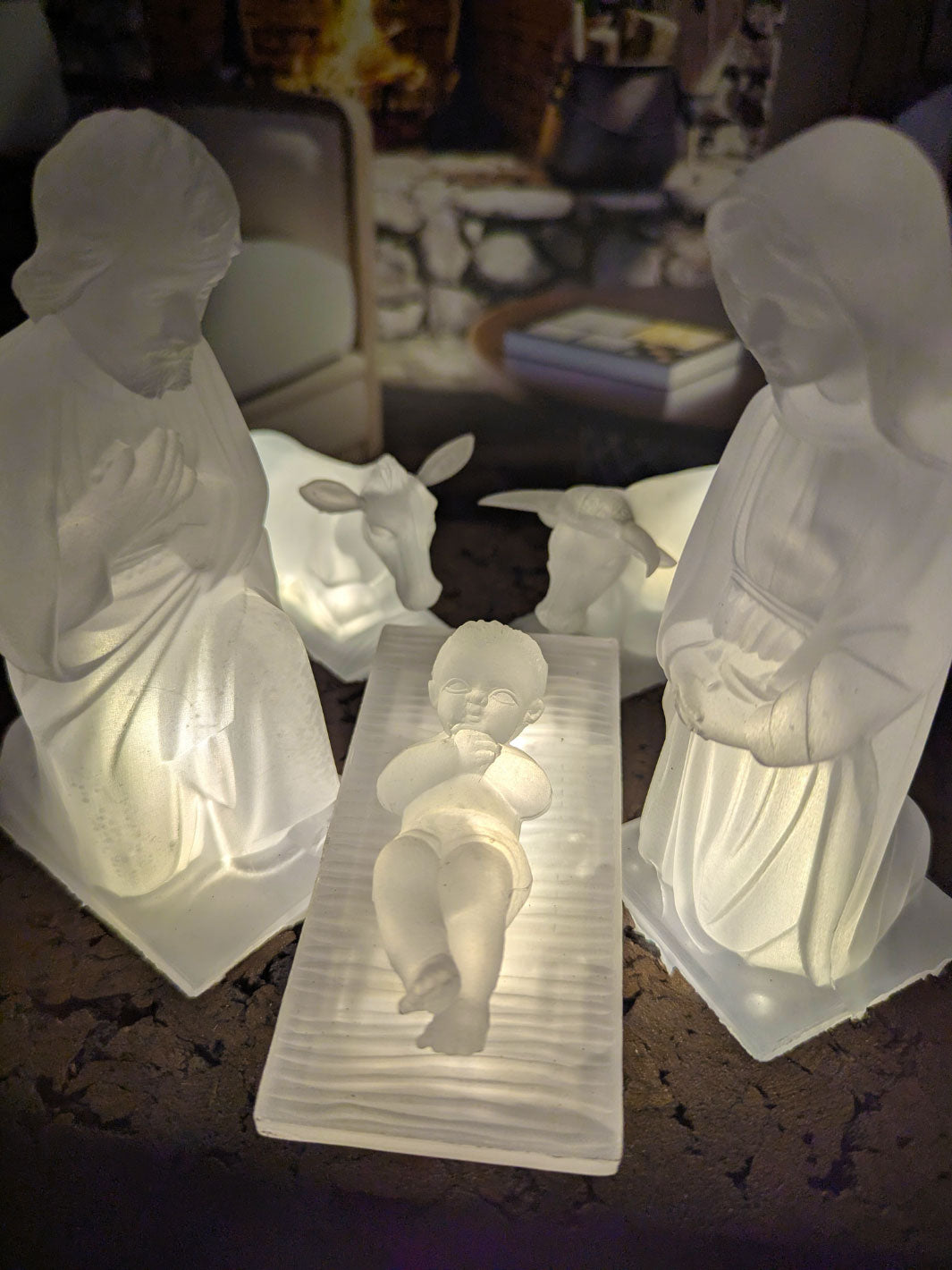 White nativity scene statues on a dark surface with a blurred indoor background