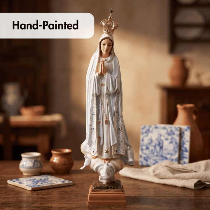 A hand-painted religious statue of the Virgin Mary standing on a base, shown on a rustic wooden table with decorative ceramic tiles and pottery in the background. A &