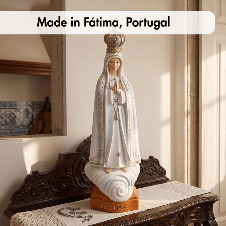 A white Virgin Mary statue with gold detailing and a crown stands on a cloud-shaped base with a wooden pedestal labeled “FÁTIMA.” It is displayed on an ornate dark wood console table in a sunlit room, with a text banner at the top reading “Made in Fátima, Portugal.