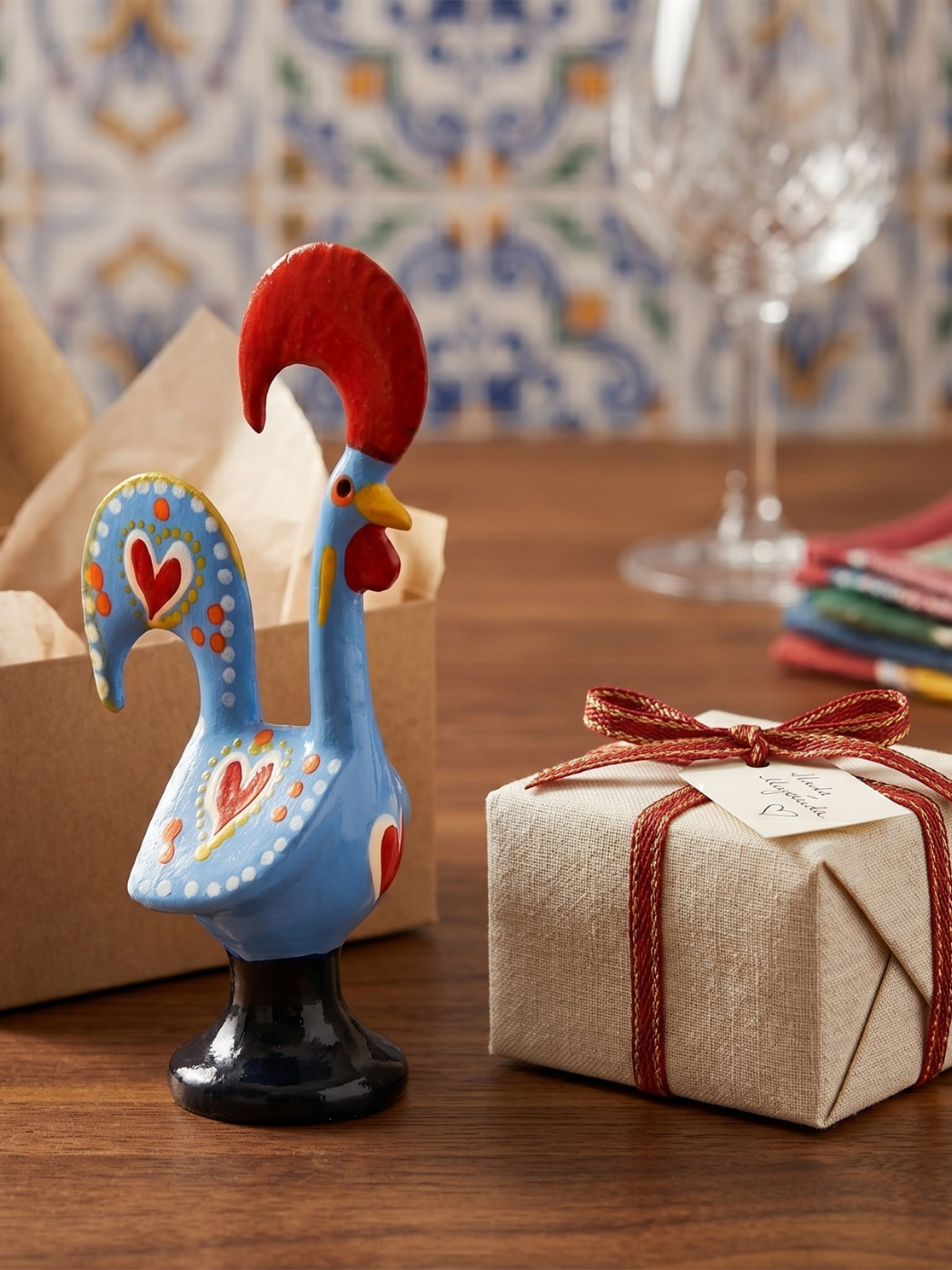 Decorative rooster figurine next to a gift box with a bow on a wooden table.