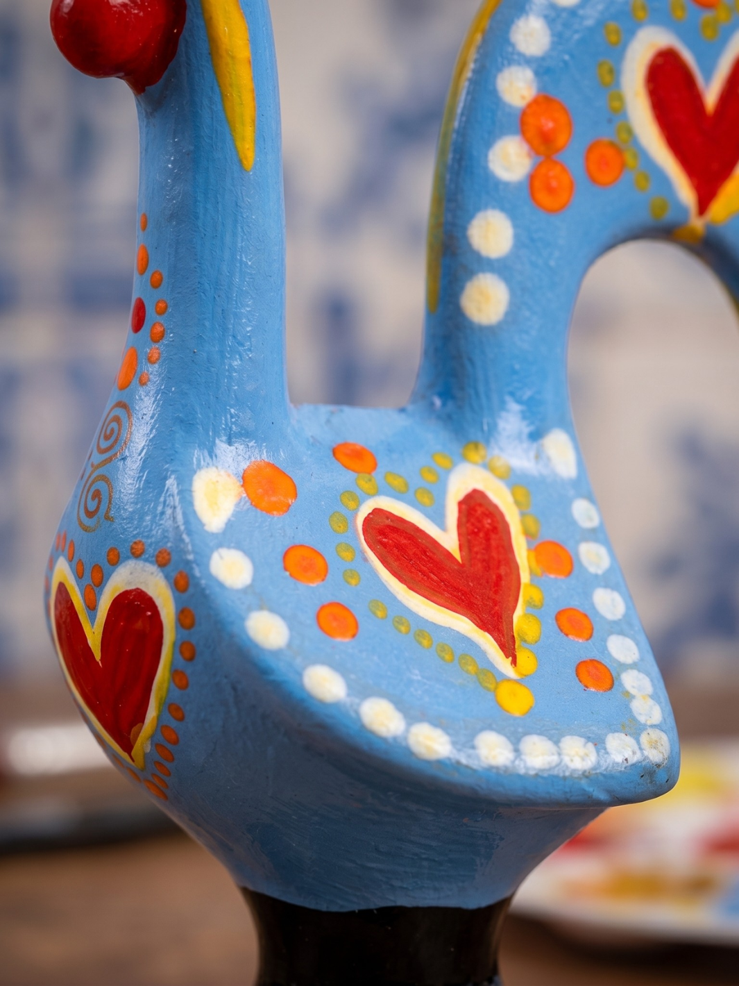 Decorative rooster figurine with blue body, red hearts, and white polka dots on a blurred background