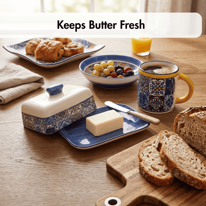 Butter dish with a pat of butter on a table with bread, fruit, and coffee.