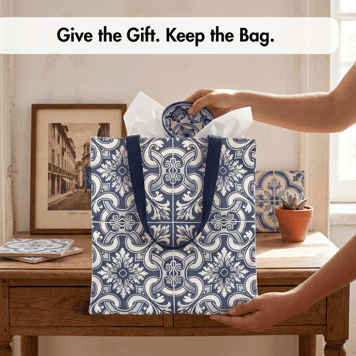 A navy blue and white patterned gift bag with dark blue handles stands on a wooden table in a home setting, with a person&