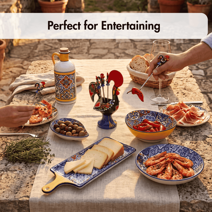 A styled outdoor dining table set with colorful ceramic serving dishes, bread, shrimp, olives, sliced cheese, cured meat, and a decorative rooster-shaped charcuterie stick holder. A hand is holding a red pepper on a metal spear, and another hand is reaching for food.