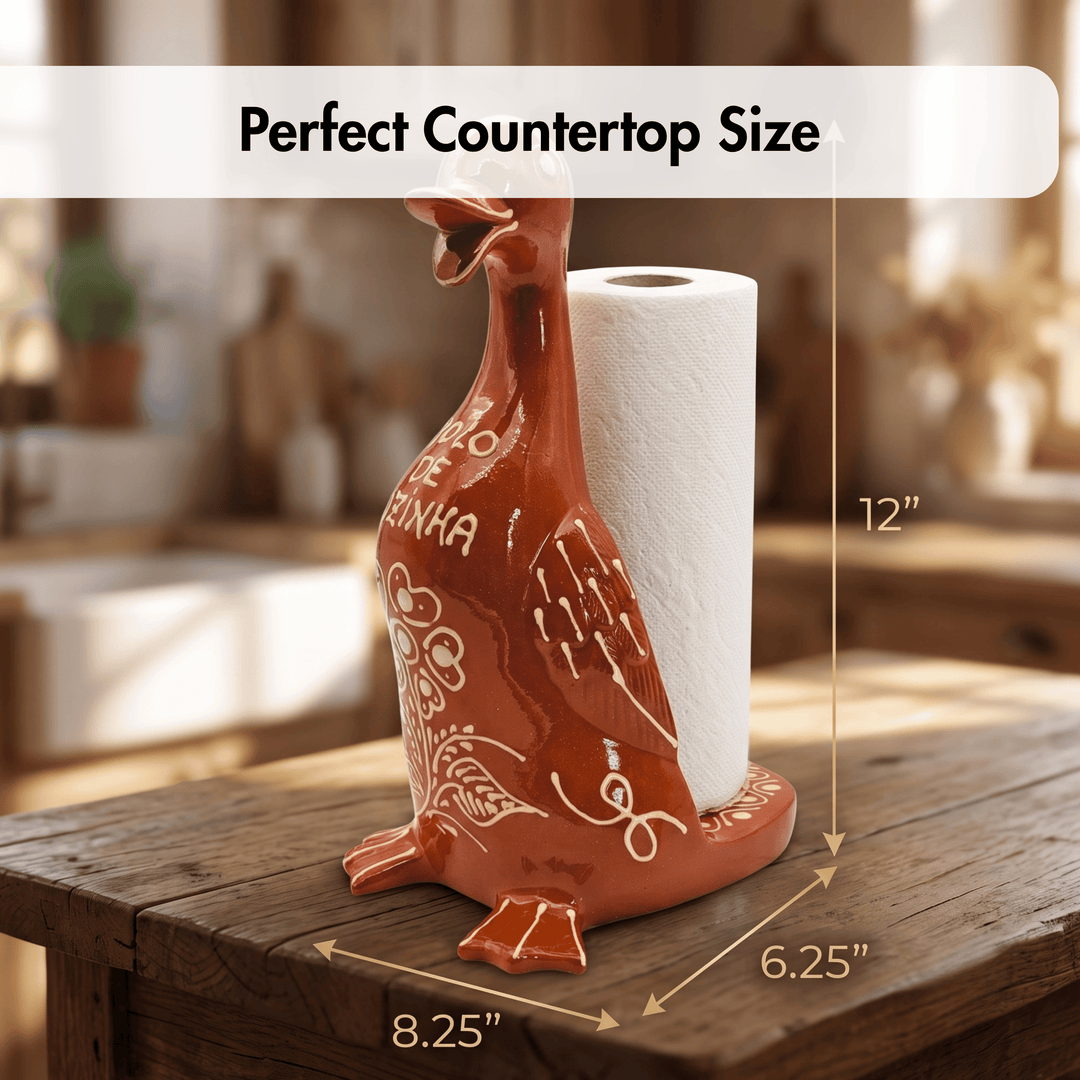 A ceramic paper towel holder shaped like a duck, shown on a wooden table in a softly blurred kitchen setting. White dimension arrows and labels indicate height, width, and depth, with a text banner reading &