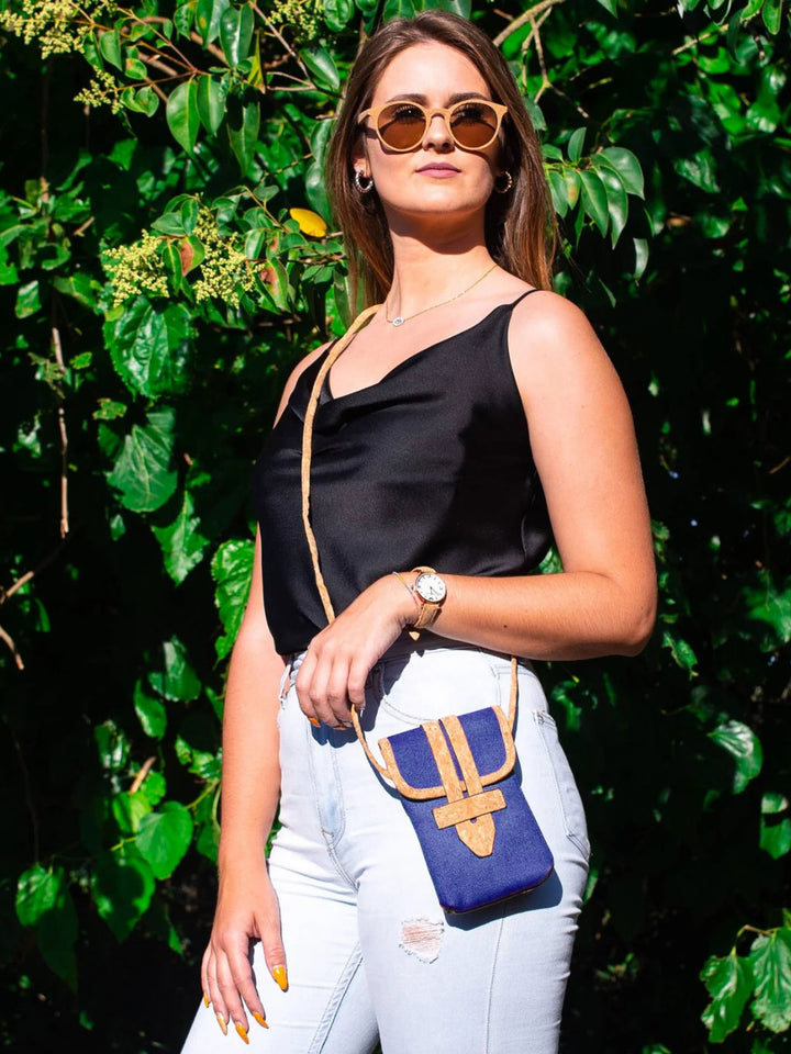 Woman holding a blue handbag with a gold logo against a green leafy background