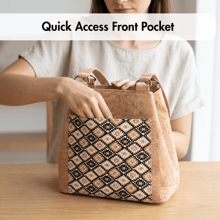 Person holding a cork handbag with a patterned front pocket on a wooden surface.