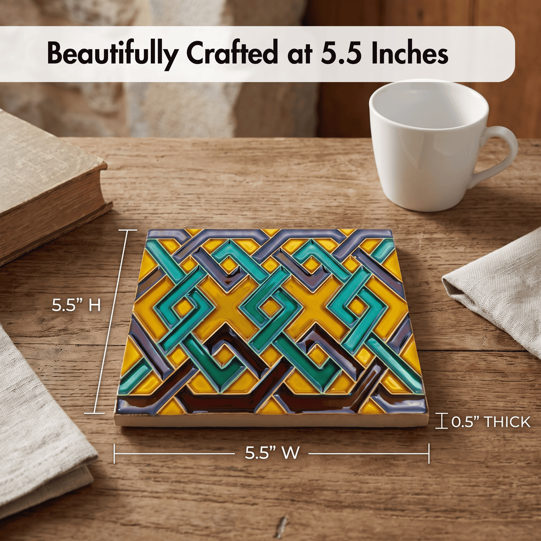 A square decorative tile with a colorful geometric interlocking pattern in yellow, teal, gray, and brown, shown on a wooden table with dimension lines indicating 5.5 inches by 5.