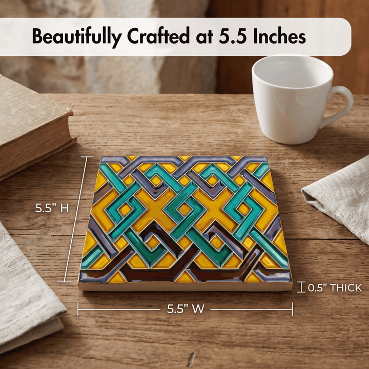 A square decorative tile with a colorful geometric interlocking pattern in yellow, teal, gray, and brown, shown on a wooden table with dimension lines indicating 5.5 inches by 5.