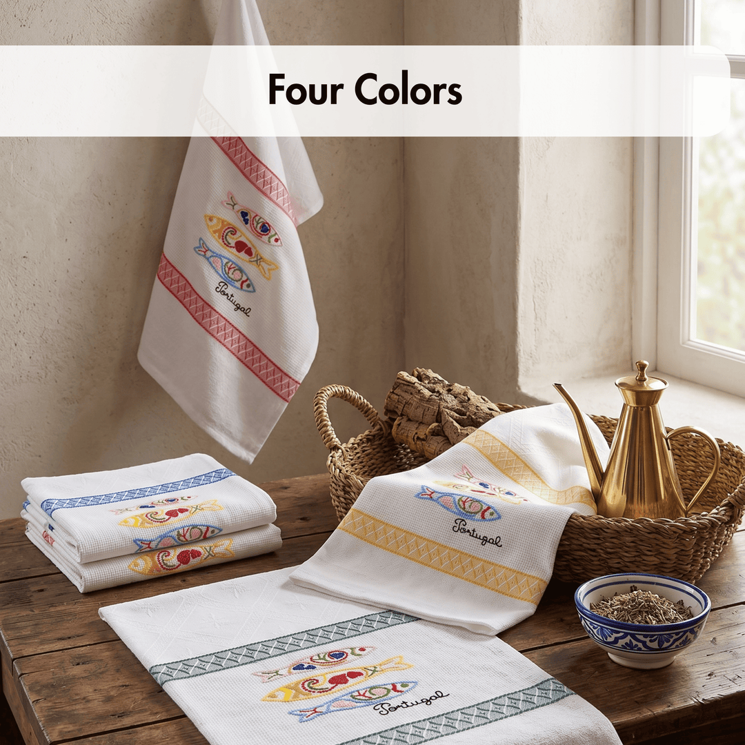 Four folded and hanging white towels with colorful embroidered fish motifs and decorative borders, arranged on a rustic wooden table beside a brass teapot, wicker basket, and bowl. A banner at the top reads &