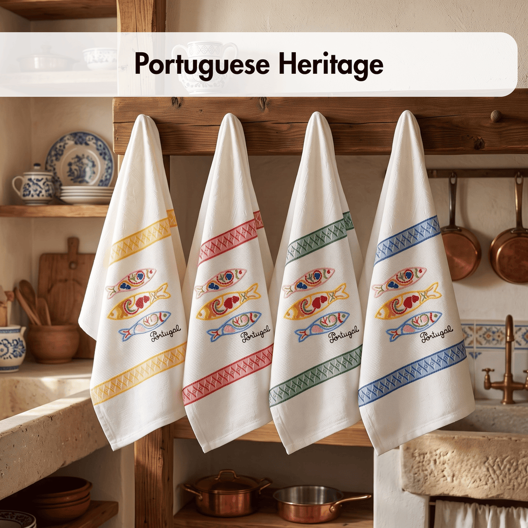 Four white kitchen towels hanging on a wooden rack in a rustic kitchen setting. Each towel features embroidered fish motifs in yellow, red, and blue, bordered by decorative stripes in gold, pink, green, and blue, with the word &