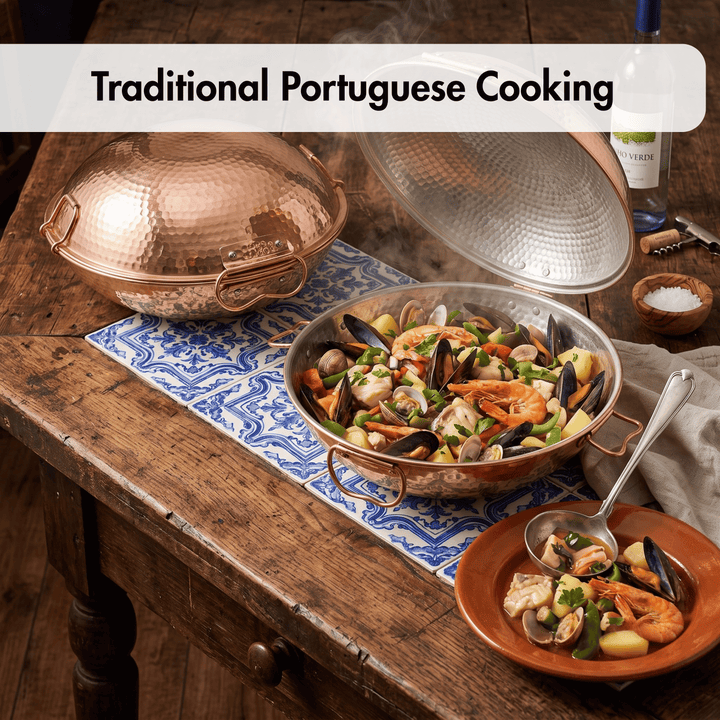 A copper paella pan filled with seafood stew sits on a rustic wooden table, with its hammered copper lid resting beside it on a blue-and-white patterned cloth. A smaller terracotta bowl with a spoon is shown in front, and the text &