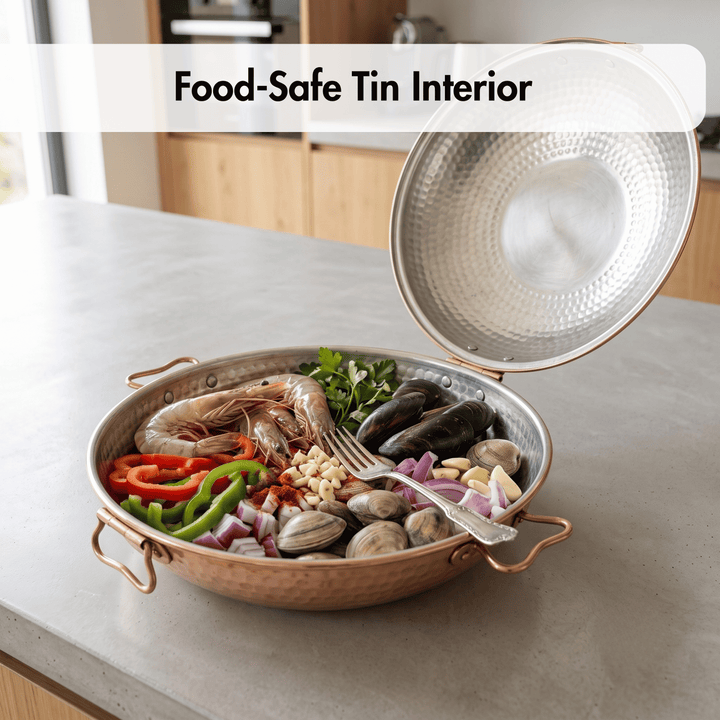 A hammered metal food pan with a copper-toned exterior and a silver textured interior, shown open on a kitchen counter with seafood and vegetables inside. Text overlay at the top reads &