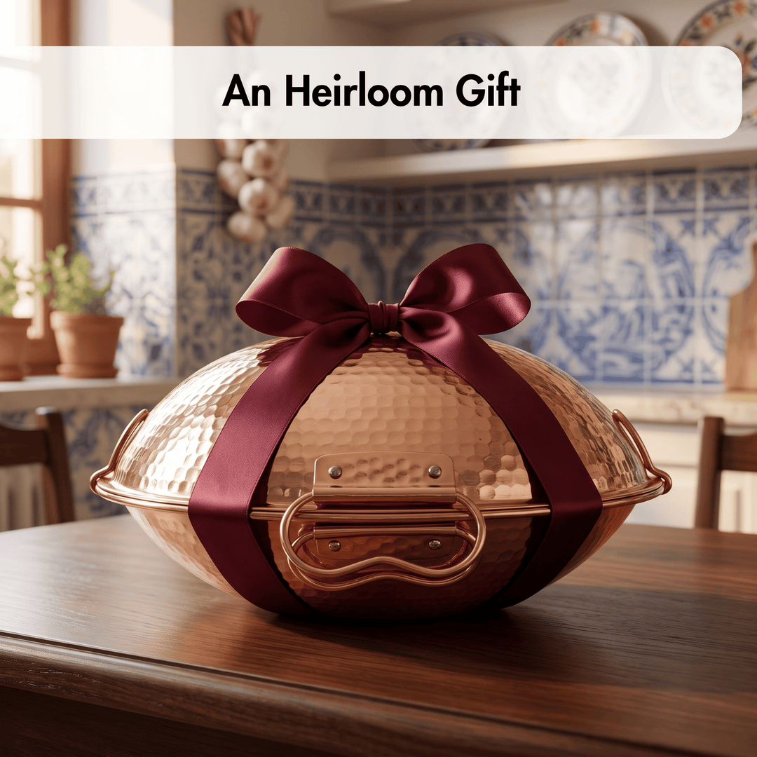A hammered copper-colored decorative gift box or vessel with a large dark burgundy ribbon bow, displayed on a wooden table in a softly blurred kitchen setting. A white banner at the top reads &