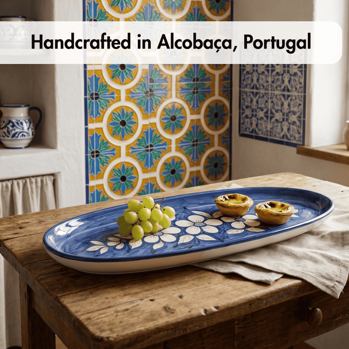 Blue decorative tray with grapes and pastries on a wooden table, with tiled wall in the background.