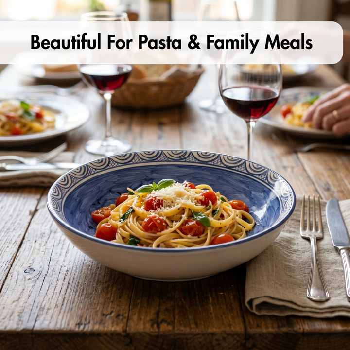 Bowl of pasta with tomatoes on a wooden table with wine glasses and cutlery.
