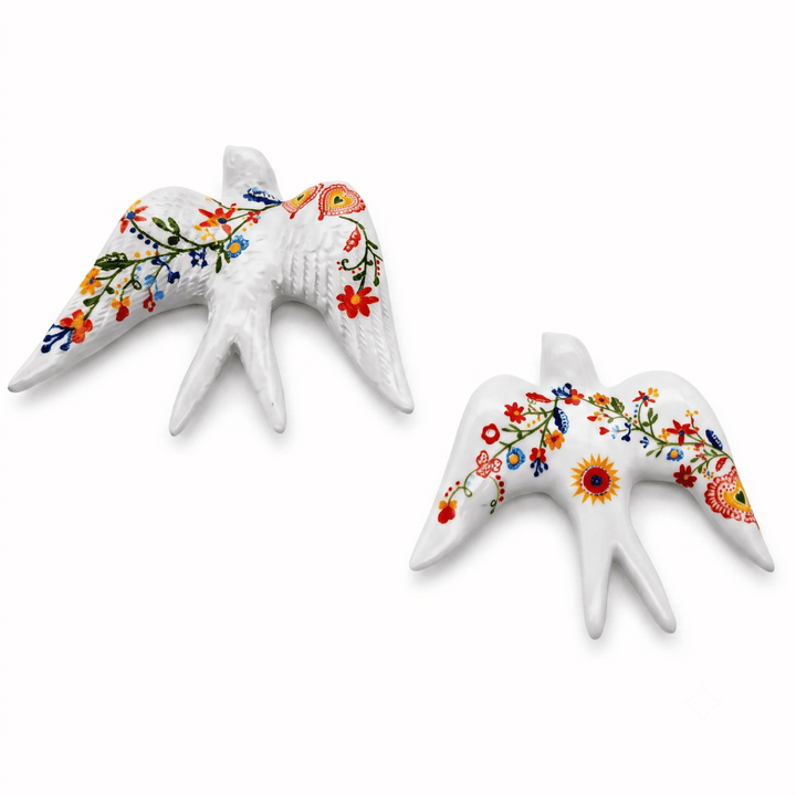 Two white ceramic swallow figurines decorated with colorful floral patterns, shown on a plain white background.