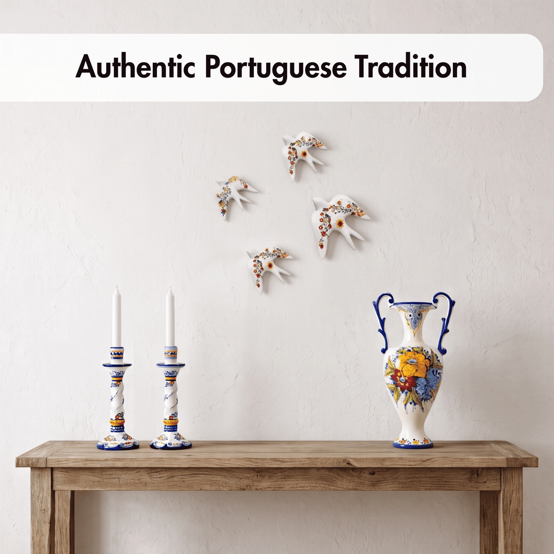 A styled interior scene showing a white ceramic vase with blue handles and colorful floral decoration on a wooden console table, alongside two matching candlesticks and small white wall-mounted bird ornaments. Text at the top reads &