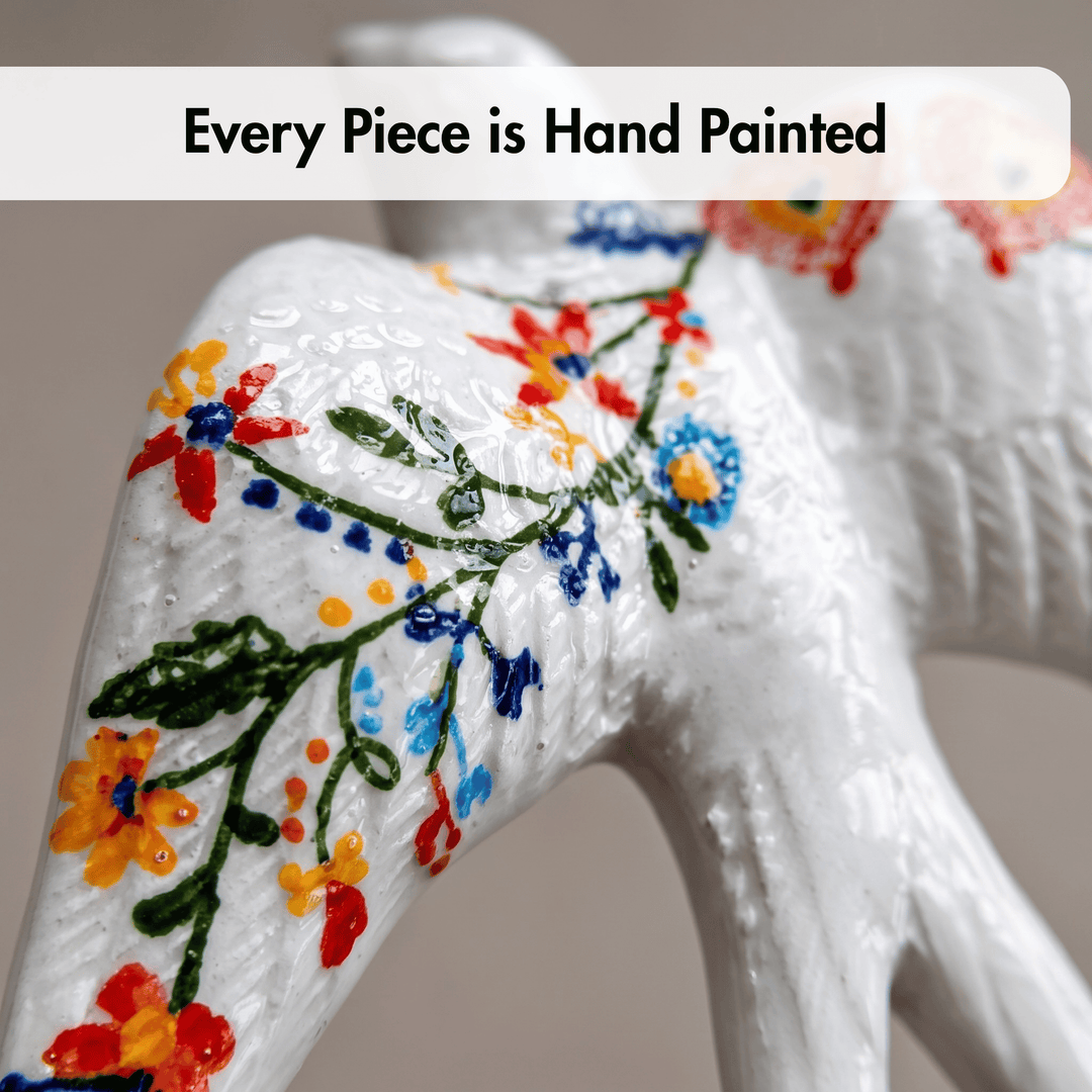 A close-up of a white ceramic decorative figurine with colorful hand-painted floral patterns, featuring a text overlay that reads &