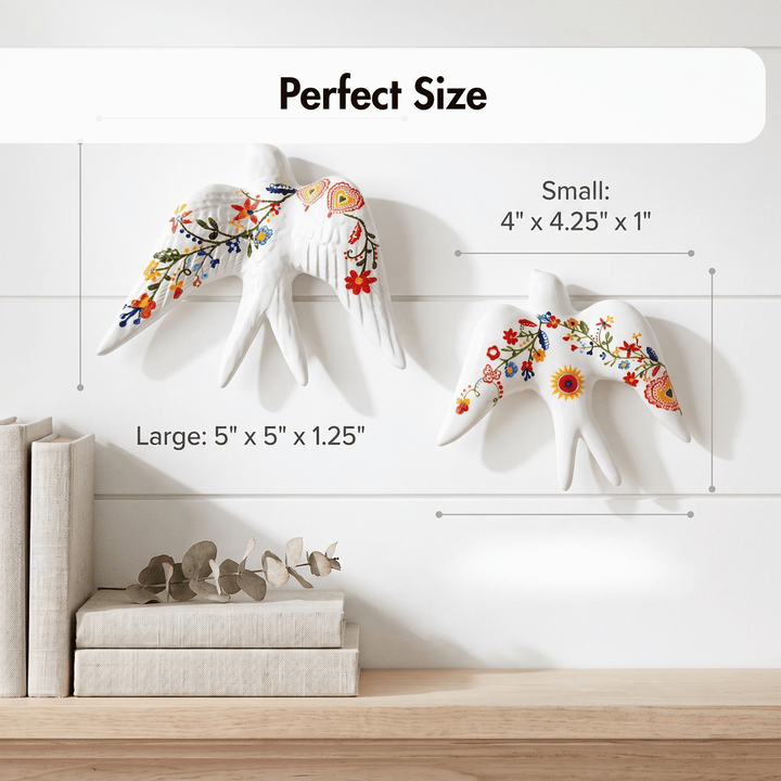Two white decorative bird wall hangings with colorful floral embroidery are shown mounted on a white wall above a wooden shelf. Text labels indicate the dimensions of each size: small 4 x 4.