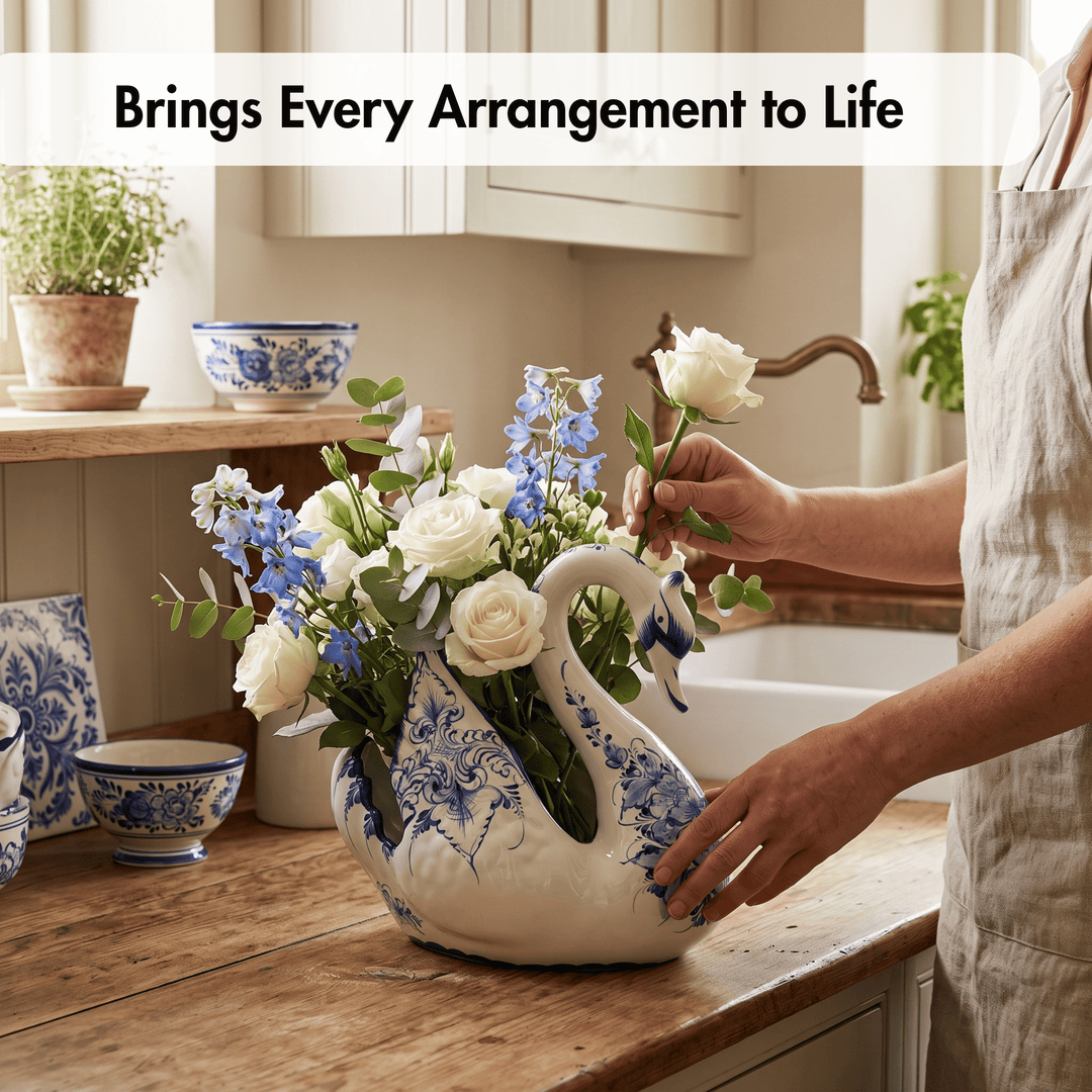 A ceramic swan-shaped flower vase with blue floral patterns sits on a wooden kitchen counter, filled with white roses, blue delphiniums, and green foliage. A person in a light beige apron is arranging the flowers, with a white farmhouse sink and cabinets in the background.