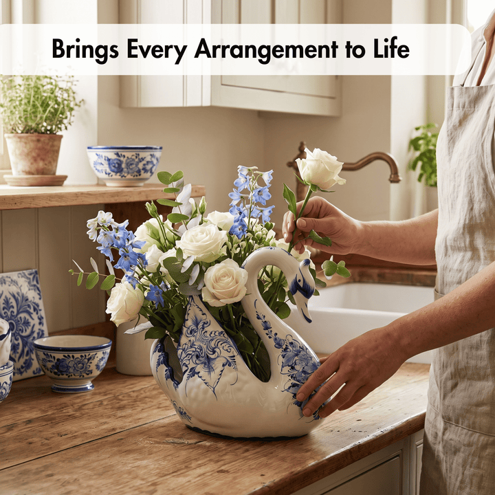 A ceramic swan-shaped flower vase with blue floral patterns sits on a wooden kitchen counter, filled with white roses, blue delphiniums, and green foliage. A person in a light beige apron is arranging the flowers, with a white farmhouse sink and cabinets in the background.