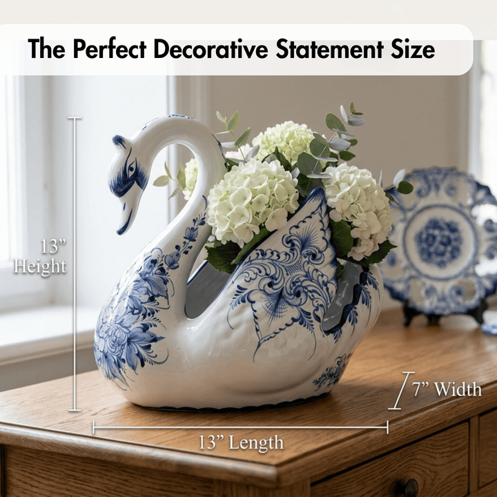 A decorative ceramic swan-shaped planter with blue floral patterns and white hydrangeas, shown on a wooden table with overlaid dimensions reading 13" height, 13" length, and 7" width. Text at the top says &