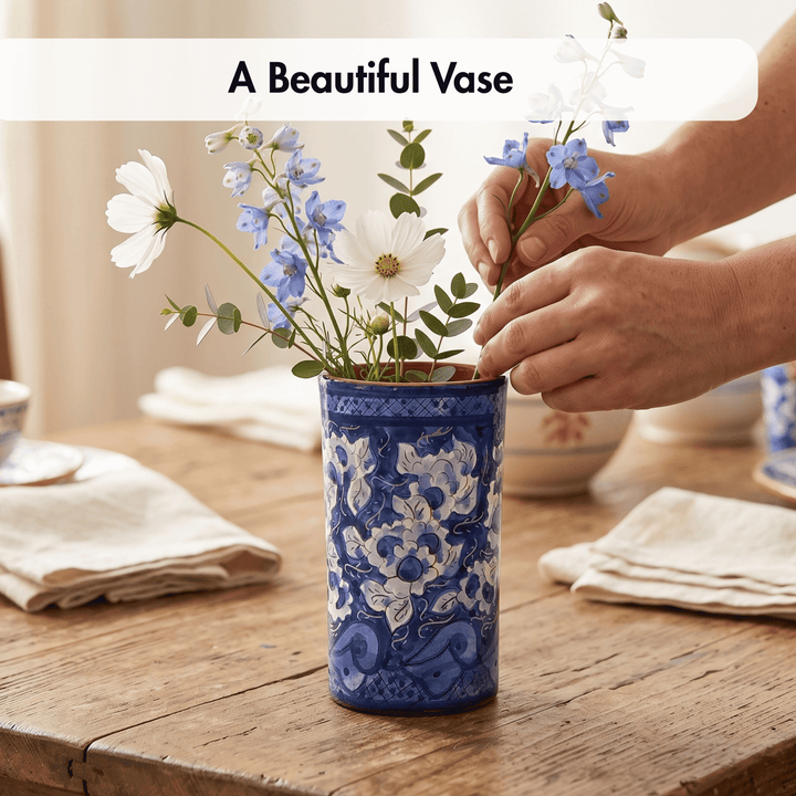 A blue and white patterned ceramic vase filled with white and blue flowers on a rustic wooden table, with a person&