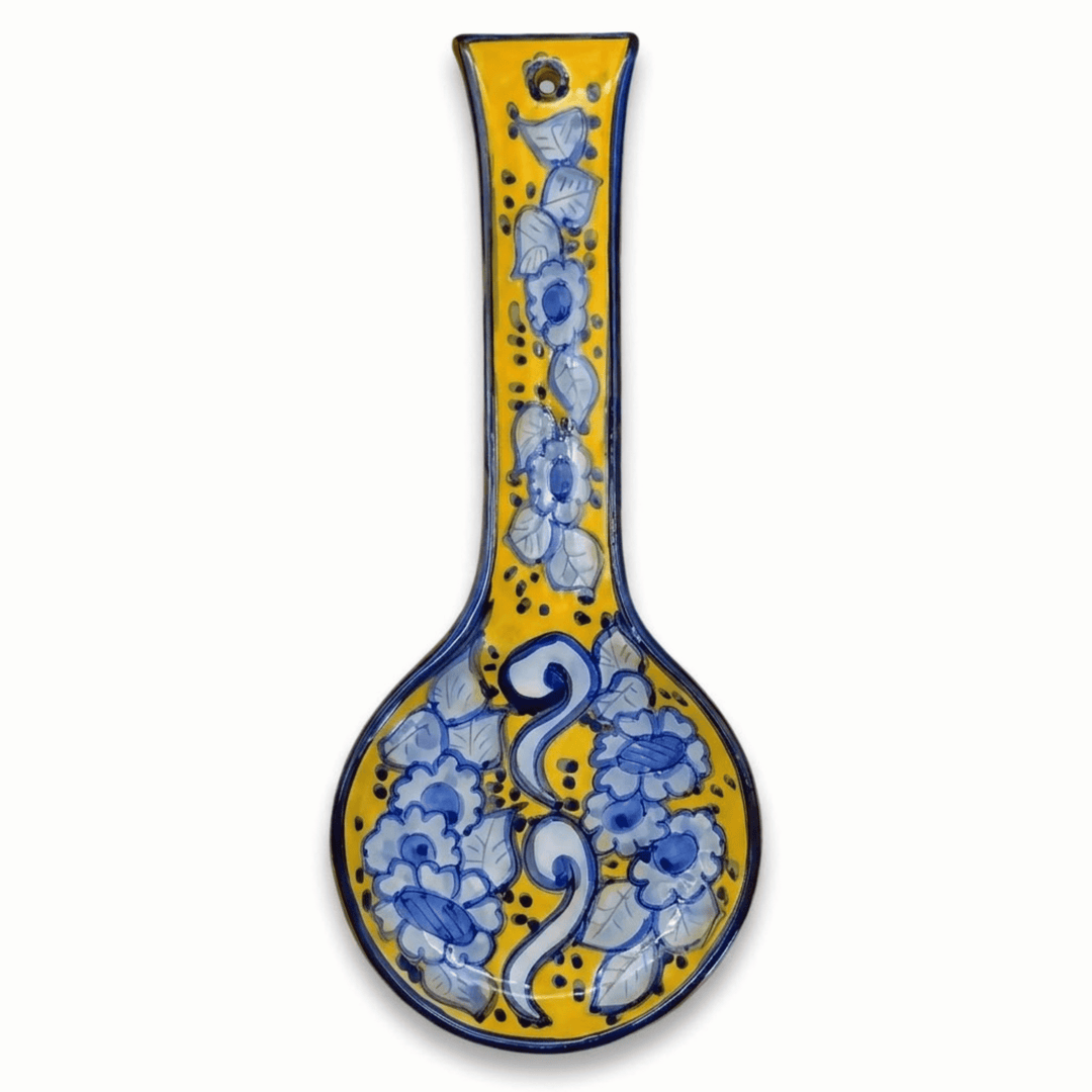 A ceramic spoon rest with a long handle and a bulbous bowl, decorated with a yellow glaze and blue floral patterns, shown on a plain white background.