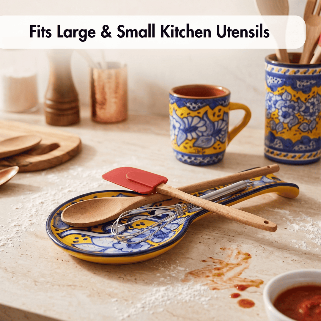 A decorative kitchen utensil holder with a blue and yellow floral pattern, shown holding wooden spoons and a red spatula on a light stone countertop. Other patterned kitchen items are blurred in the background, and the text &