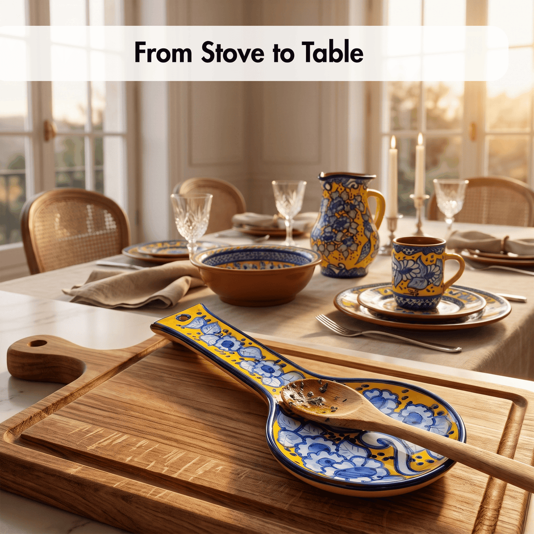 A styled dining table set with matching ceramic tableware in a warm indoor setting. In the foreground, a wooden spoon rests on a blue and yellow patterned serving spoon rest with a matching plate, while the background shows a pitcher, bowls, cups, and plates on a set dining table with candles and glassware.