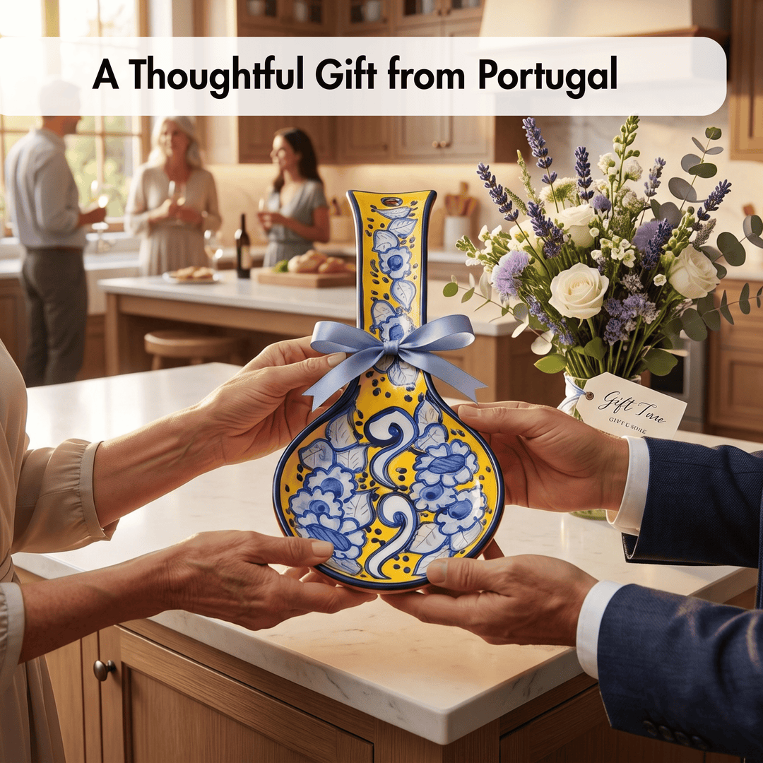 A handcrafted Portuguese ceramic vase with a yellow and blue floral pattern, held by two people in a bright kitchen setting. A blue ribbon is tied around the neck of the vase.