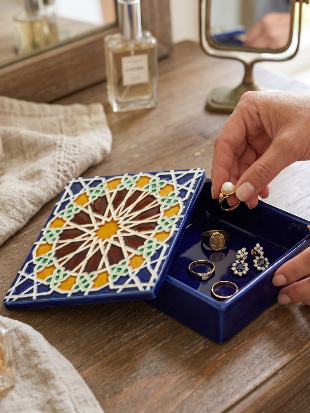 Person organizing jewelry in a decorative blue jewelry box on a wooden surface.