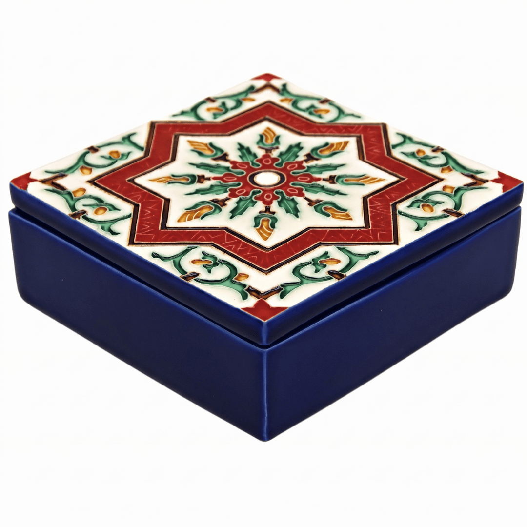A square ceramic keepsake box with a dark blue base and a lid decorated with a red, green, and gold geometric star pattern on a white background.