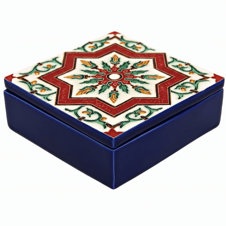 A square ceramic keepsake box with a dark blue base and a lid decorated with a red, green, and gold geometric star pattern on a white background.