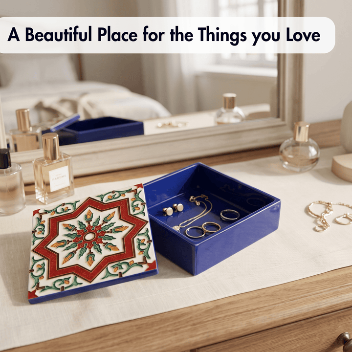 A blue jewelry box with a decorative multicolor patterned lid sits open on a wooden dresser next to perfume bottles and jewelry. A text overlay at the top reads, &
