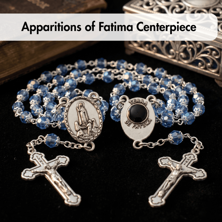 Blue beaded rosary with silver accents on a dark surface, labeled 'Apparitions of Fatima Centerpiece'.