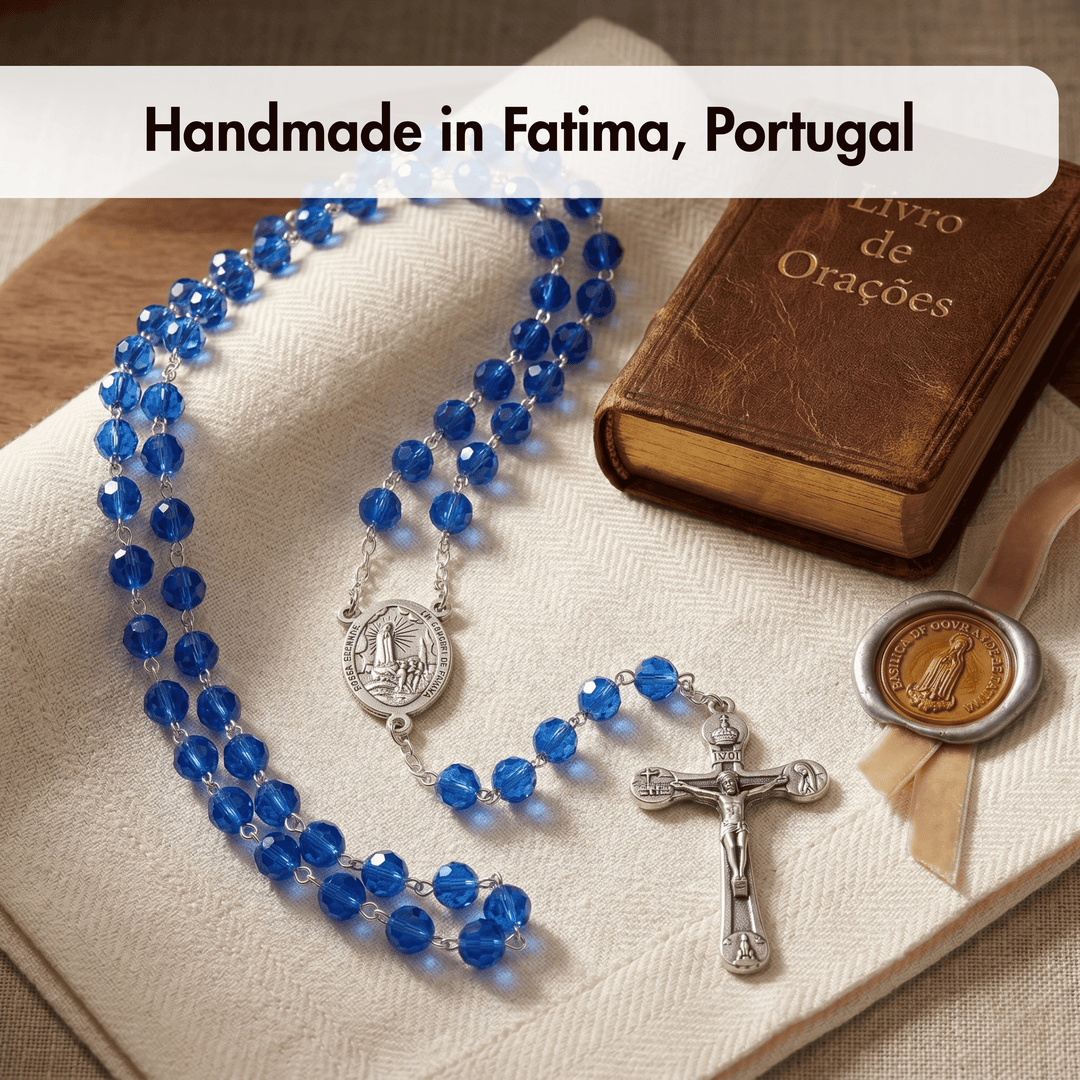 Blue rosary with silver crucifix and medal on a brown book, with text 'Handmade in Fatima, Portugal'.