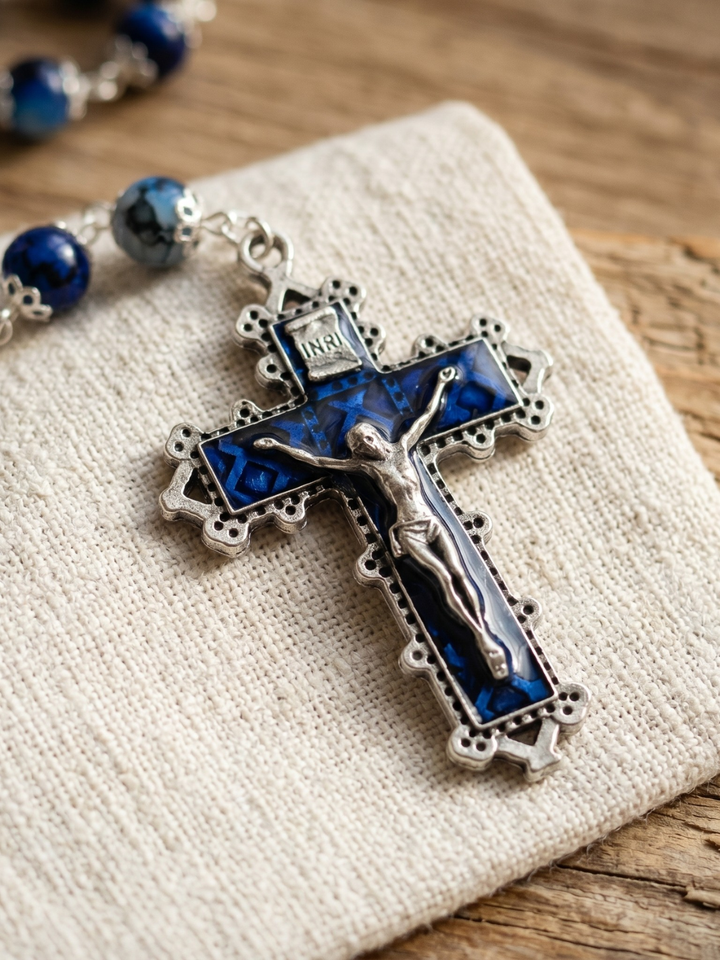 Silver cross pendant with blue accents on a textured fabric surface
