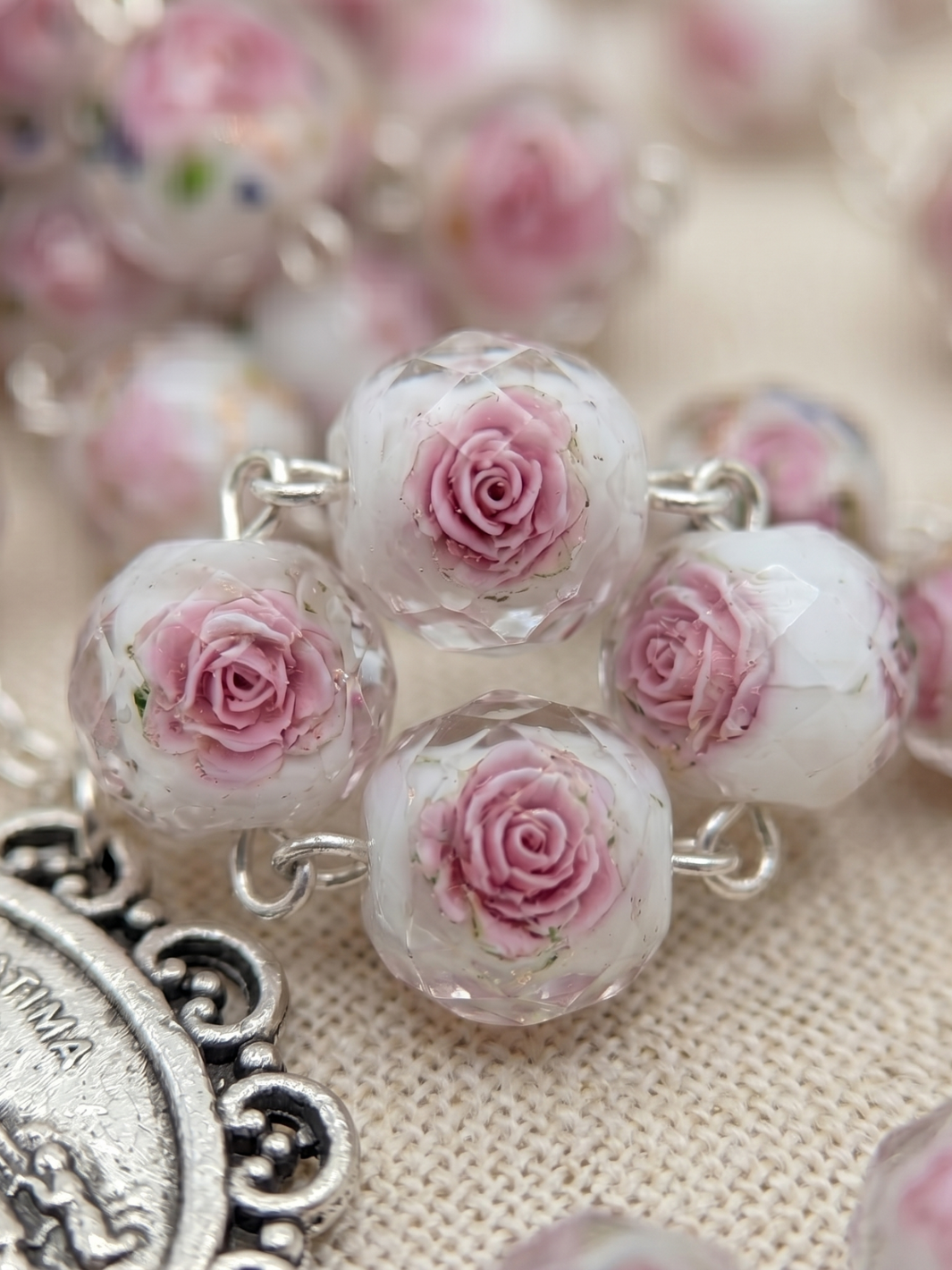 Close-up of a rosary with pink rose beads on a textured surface